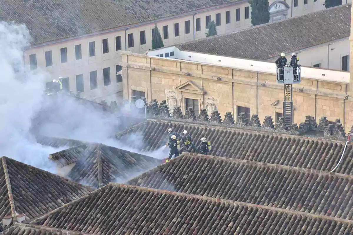 Bomberos trabajando sobre un tejado antiguo cubierto de humo mientras intentan apagar un incendio en un edificio histórico