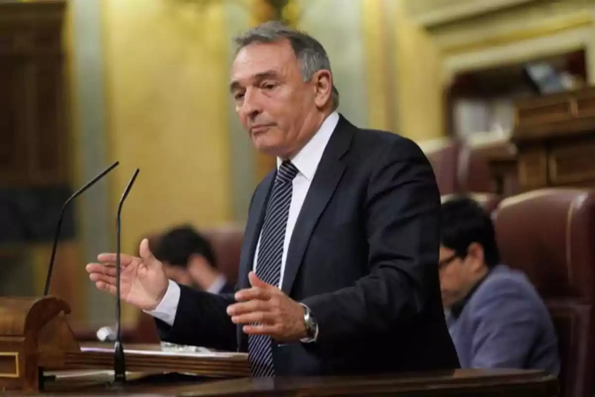 Hombre de traje hablando en un podio dentro de un recinto parlamentario Hombre de traje hablando en un podio dentro de un recinto parlamentario