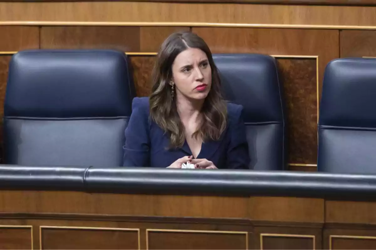 Mujer sentada en un escaño de un parlamento con expresión seria y las manos entrelazadas Mujer sentada en un escaño de un parlamento con expresión seria y las manos entrelazadas