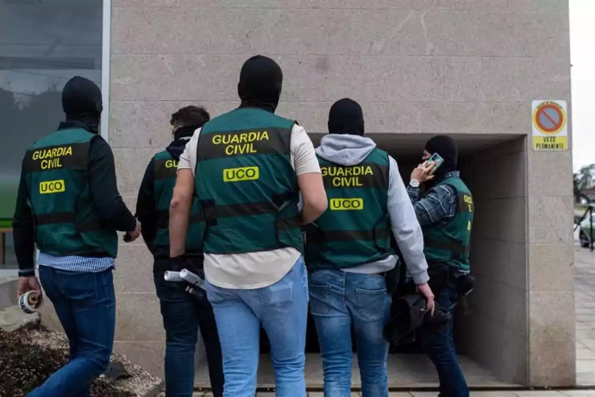 Varios agentes de la Guardia Civil con chalecos identificativos y pasamontañas entran a un edificio mientras uno de ellos habla por teléfono móvil. Varios agentes de la Guardia Civil con chalecos identificativos y pasamontañas entran a un edificio mientras uno de ellos habla por teléfono móvil.