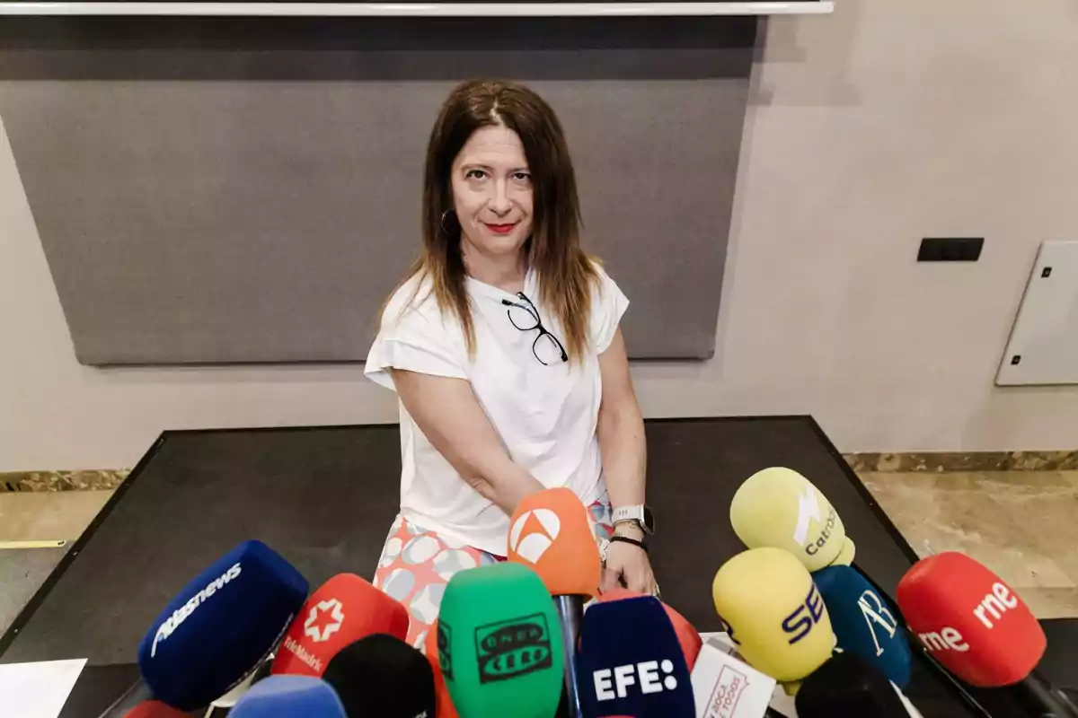 Mujer sentada frente a varios micrófonos de diferentes medios de comunicación en una sala de conferencias Mujer sentada frente a varios micrófonos de diferentes medios de comunicación en una sala de conferencias