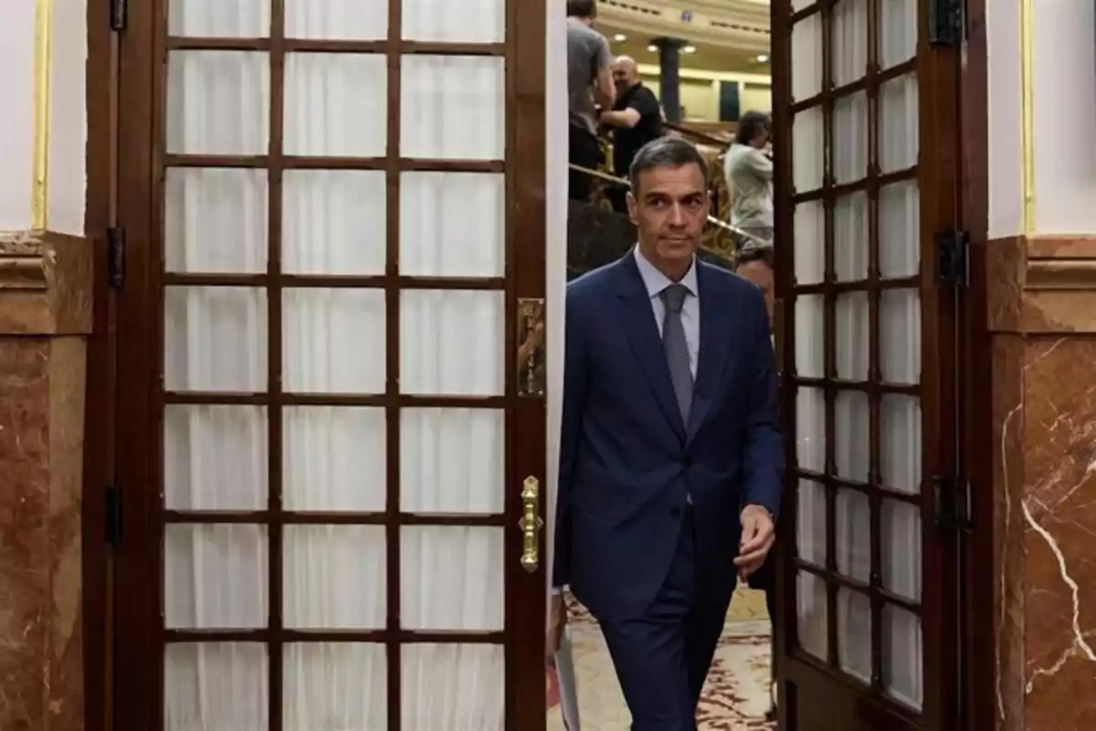 Hombre con traje azul entrando por una puerta de madera con cristales en un edificio elegante