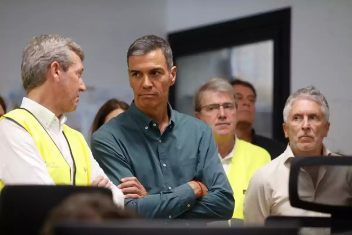 Varios hombres de pie en una sala, algunos con chaleco amarillo, observando atentamente algo fuera de la imagen Varios hombres de pie en una sala, algunos con chaleco amarillo, observando atentamente algo fuera de la imagen