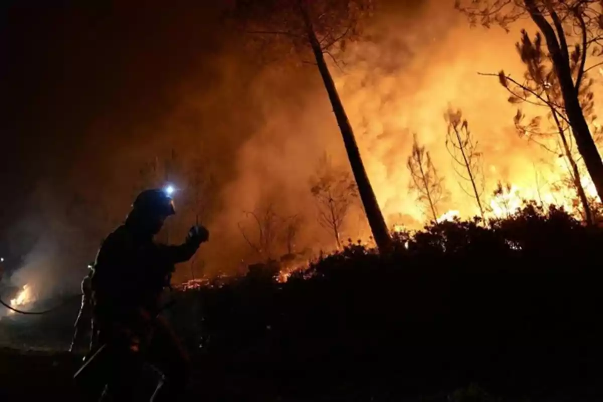 Bombero con casco y linterna lucha contra un incendio forestal de gran magnitud durante la noche