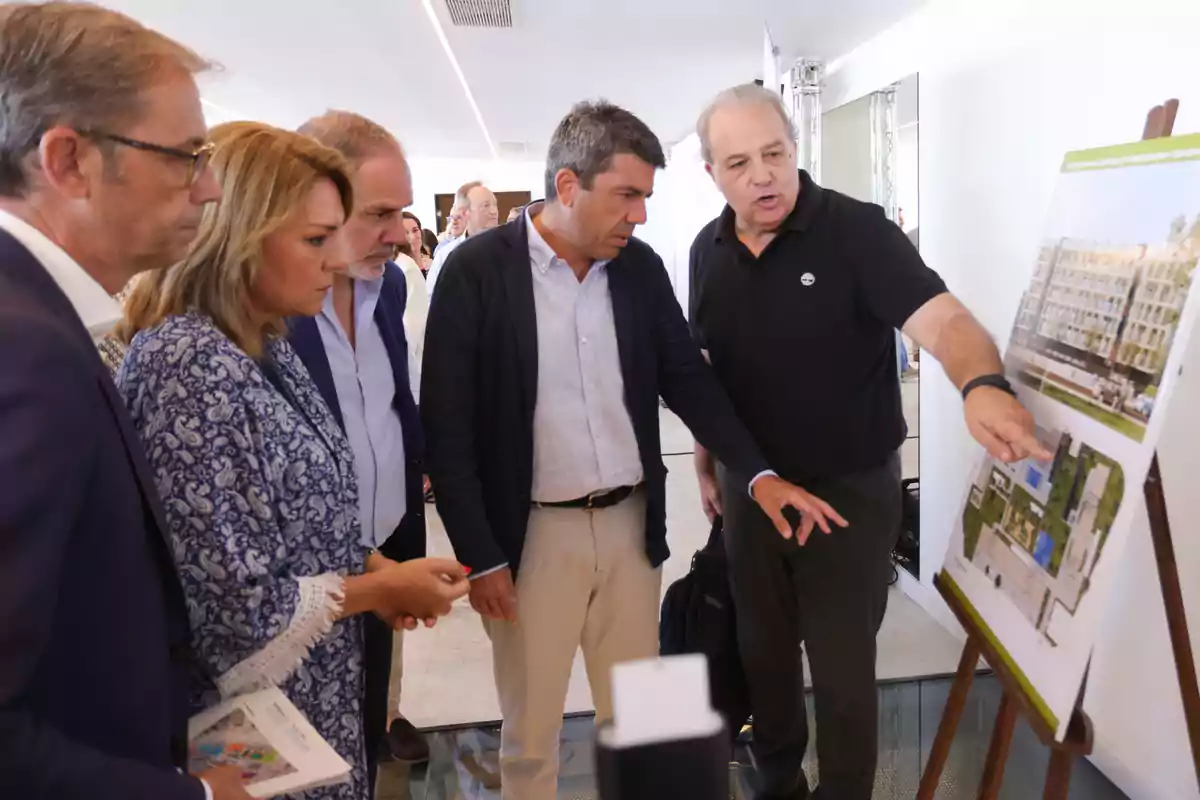 Un grupo de personas observa atentamente un plano arquitectónico expuesto en un caballete mientras un hombre señala detalles del diseño
