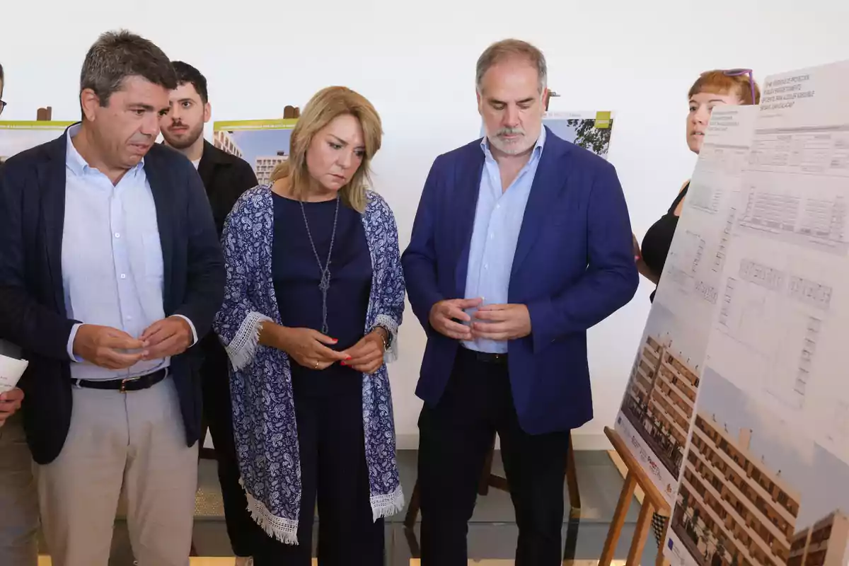 Varias personas observan atentamente unos paneles con planos y fotografías de un edificio en una exposición o presentación arquitectónica. Varias personas observan atentamente unos paneles con planos y fotografías de un edificio en una exposición o presentación arquitectónica.
