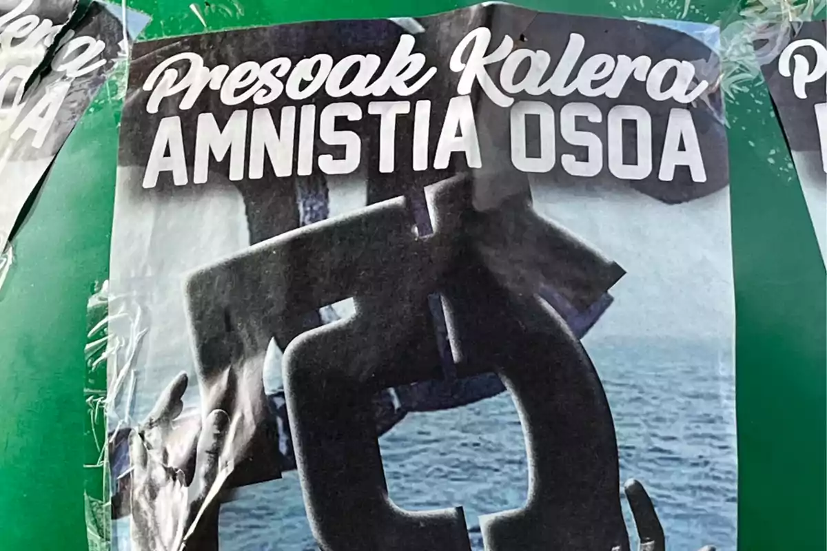 Cartel con el texto Presoak Kalera Amnistia Osoa sobre una imagen de unas esposas abiertas y el mar de fondo