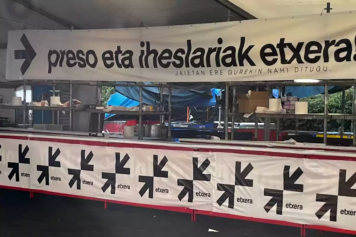 Puesto de comida decorado con pancartas que tienen mensajes en euskera y flechas negras junto a la palabra etxera Puesto de comida decorado con pancartas que tienen mensajes en euskera y flechas negras junto a la palabra etxera