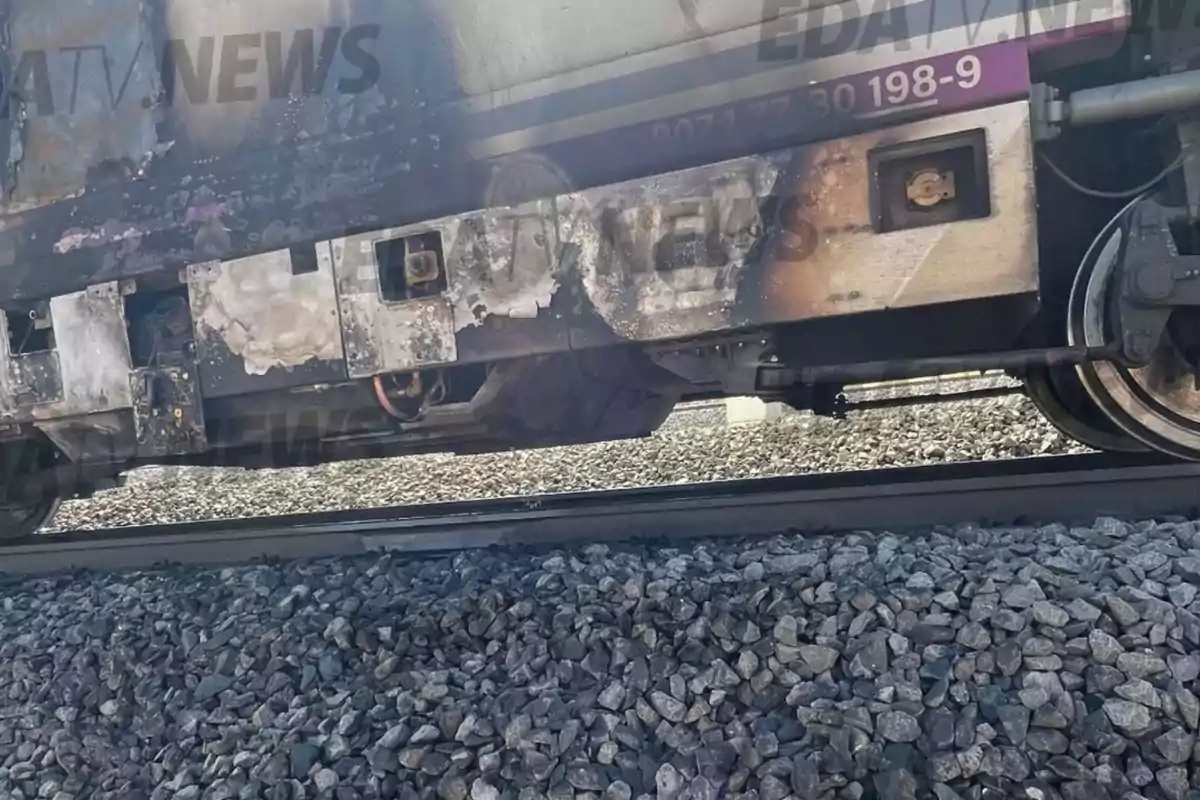Parte inferior de un vagón de tren con marcas de quemaduras y daños visibles sobre las vías rodeadas de piedras. Parte inferior de un vagón de tren con marcas de quemaduras y daños visibles sobre las vías rodeadas de piedras.