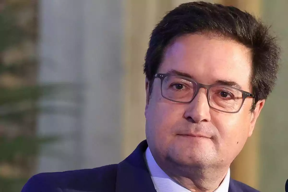 Hombre de cabello oscuro y gafas con expresión seria vestido con saco azul en un entorno interior desenfocado Hombre de cabello oscuro y gafas con expresión seria vestido con saco azul en un entorno interior desenfocado