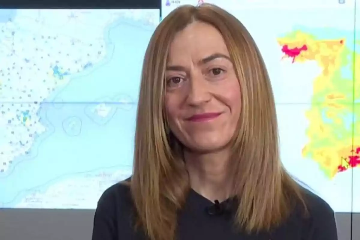 Mujer de cabello lacio y rubio oscuro sonriendo frente a un mapa meteorológico en una pantalla Mujer de cabello lacio y rubio oscuro sonriendo frente a un mapa meteorológico en una pantalla