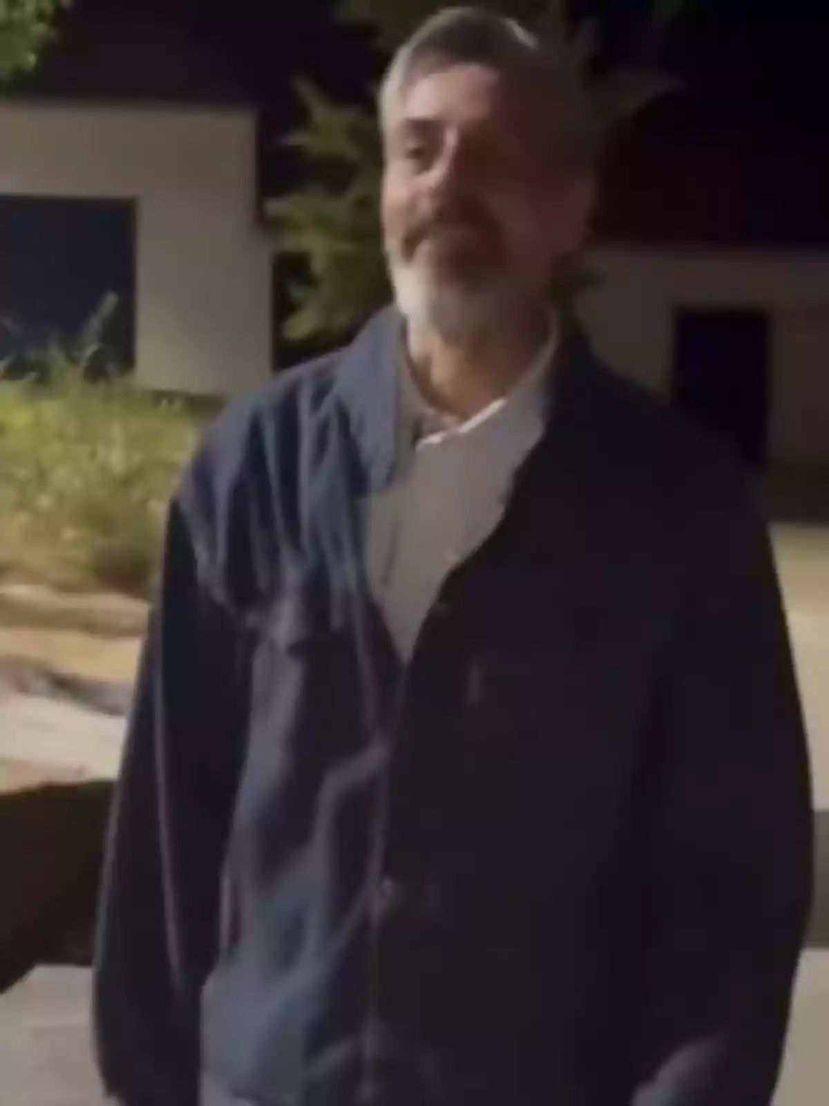 Hombre de cabello canoso y barba con chaqueta oscura de pie al aire libre durante la noche Hombre de cabello canoso y barba con chaqueta oscura de pie al aire libre durante la noche