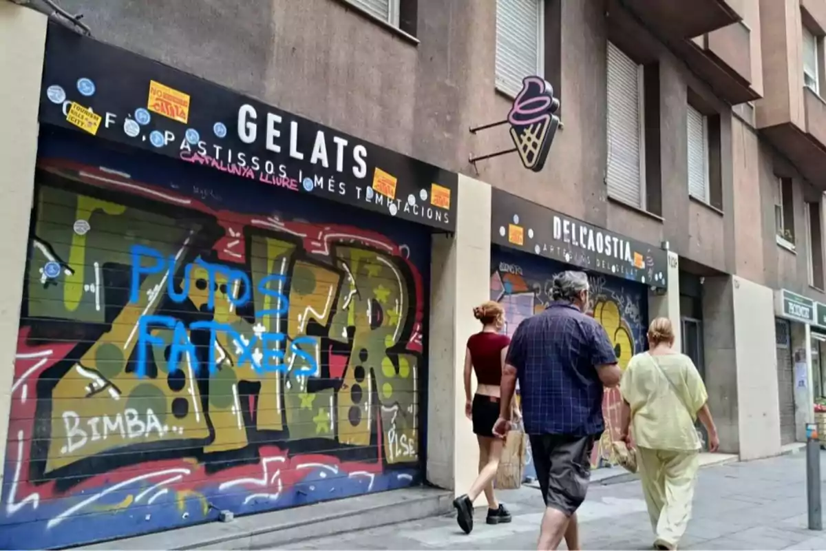 Personas caminando por una acera frente a una heladería cerrada con persianas cubiertas de grafitis y pegatinas Personas caminando por una acera frente a una heladería cerrada con persianas cubiertas de grafitis y pegatinas