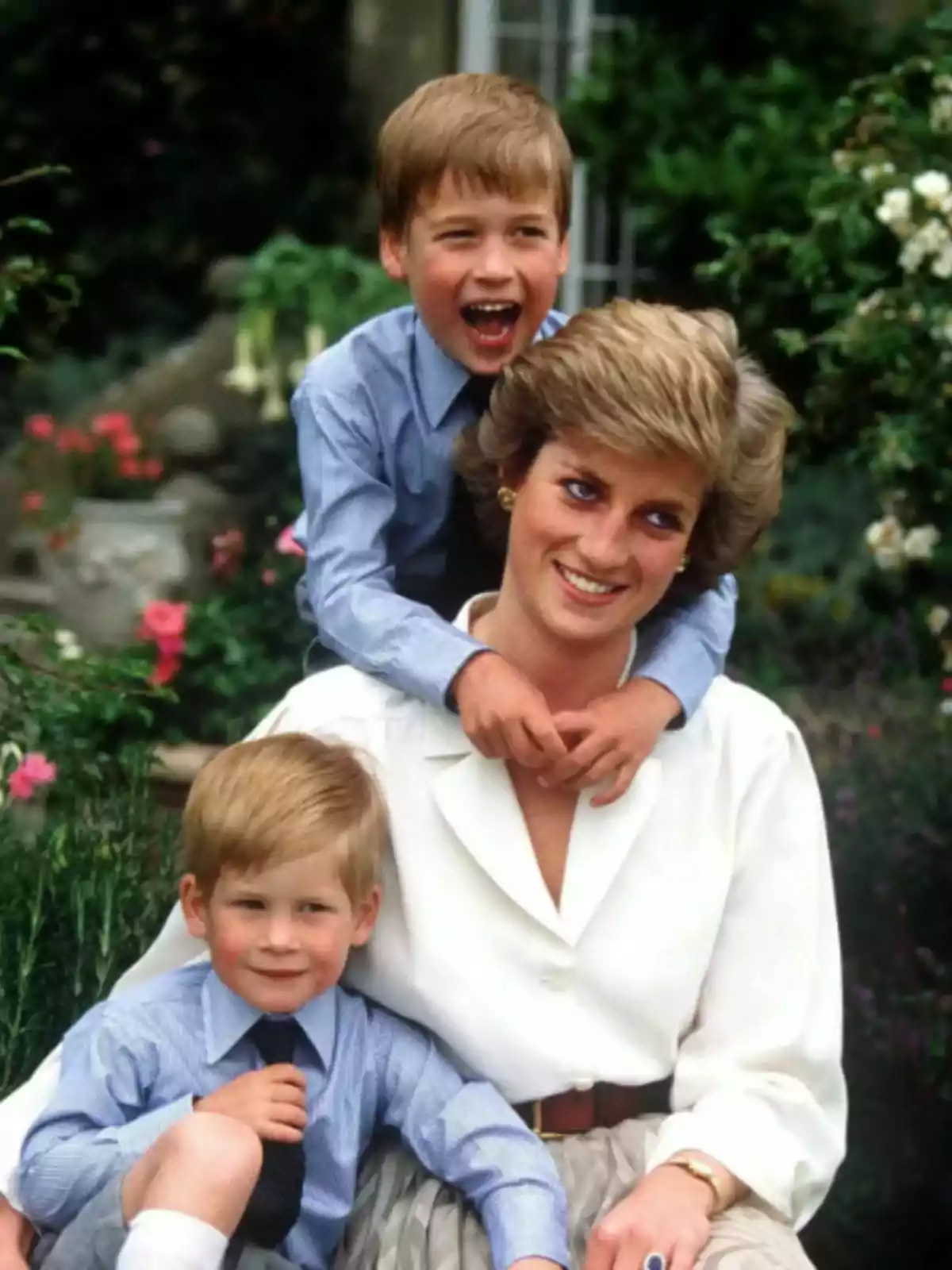 Lady Di sonriente sentada en un jardín con los príncipes Guillermo y Harry abrazándola, todos vestidos de manera elegante y rodeados de flores. Lady Di sonriente sentada en un jardín con los príncipes Guillermo y Harry abrazándola, todos vestidos de manera elegante y rodeados de flores.