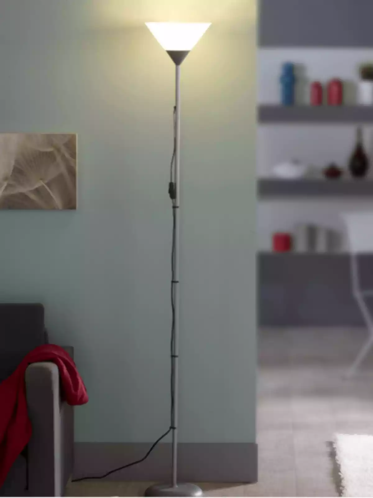 Lámpara de pie encendida junto a un sofá gris con una manta roja en una sala moderna Lámpara de pie encendida junto a un sofá gris con una manta roja en una sala moderna