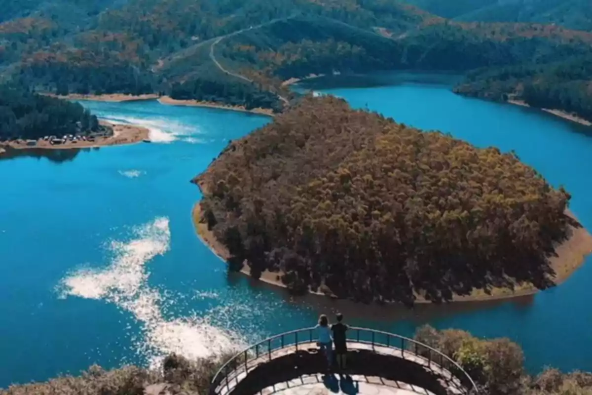 Pareja observando una isla con forma de corazón rodeada de agua azul y vegetación desde un mirador elevado Pareja observando una isla con forma de corazón rodeada de agua azul y vegetación desde un mirador elevado
