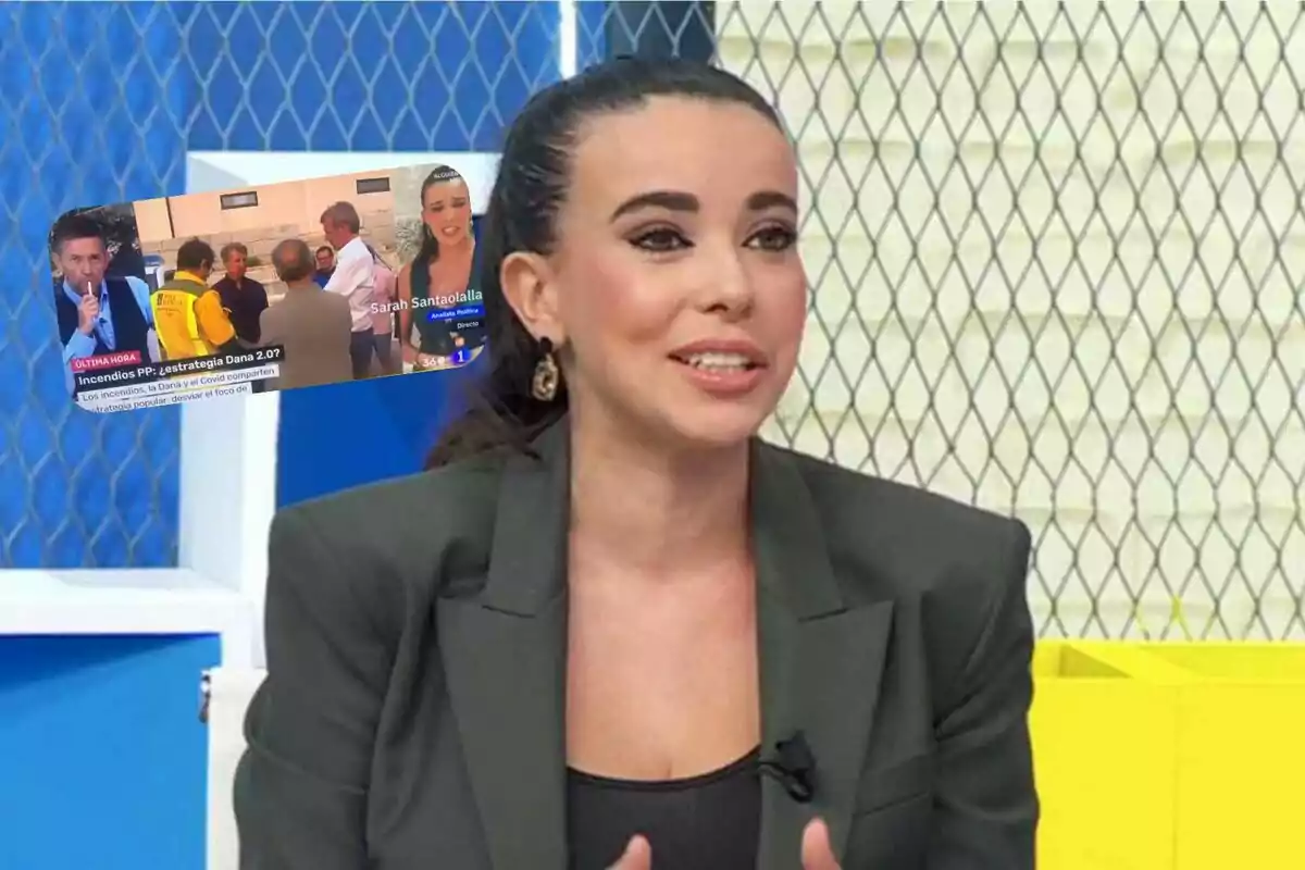 Una mujer de cabello oscuro recogido y chaqueta gris habla en un set de televisión con fondo de malla metálica y colores azul y amarillo, mientras en la esquina superior izquierda aparece una captura de pantalla de un noticiero con varias personas y una reportera
