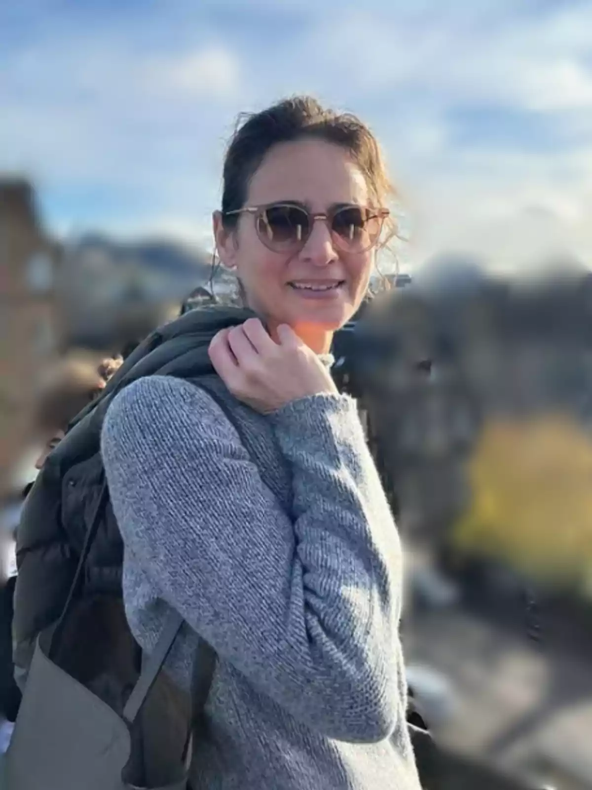 Woman wearing sunglasses and a gray sweater smiling outdoors with a blurred urban background Woman wearing sunglasses and a gray sweater smiling outdoors with a blurred urban background