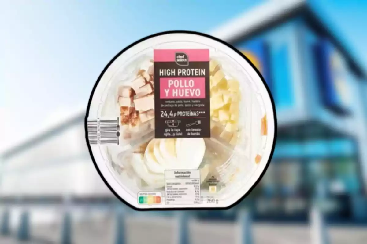 Envase redondo de ensalada alta en proteína con pollo, huevo y queso, con etiqueta en español y fondo de supermercado desenfocado Envase redondo de ensalada alta en proteína con pollo, huevo y queso, con etiqueta en español y fondo de supermercado desenfocado