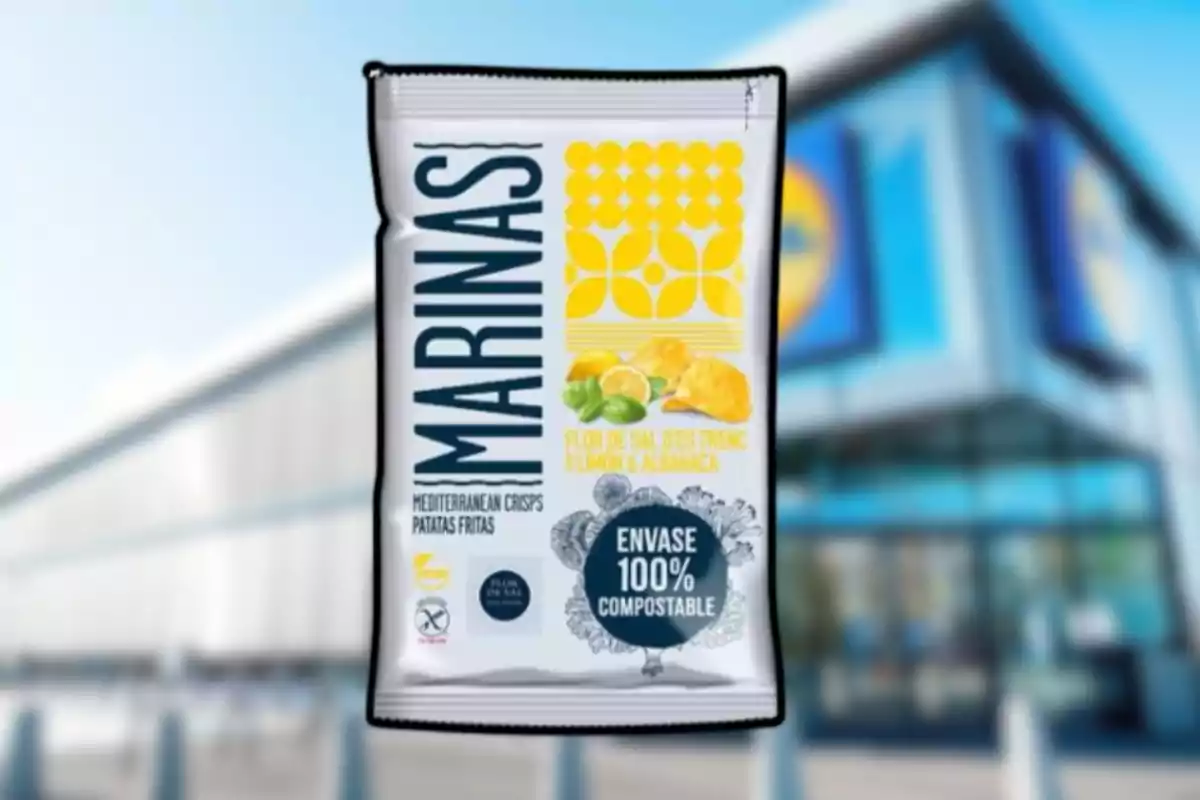 Bolsa de patatas fritas Marinas con sabor a limón y albahaca, envase 100% compostable, frente a una tienda con fachada azul y amarilla desenfocada. Bolsa de patatas fritas Marinas con sabor a limón y albahaca, envase 100% compostable, frente a una tienda con fachada azul y amarilla desenfocada.