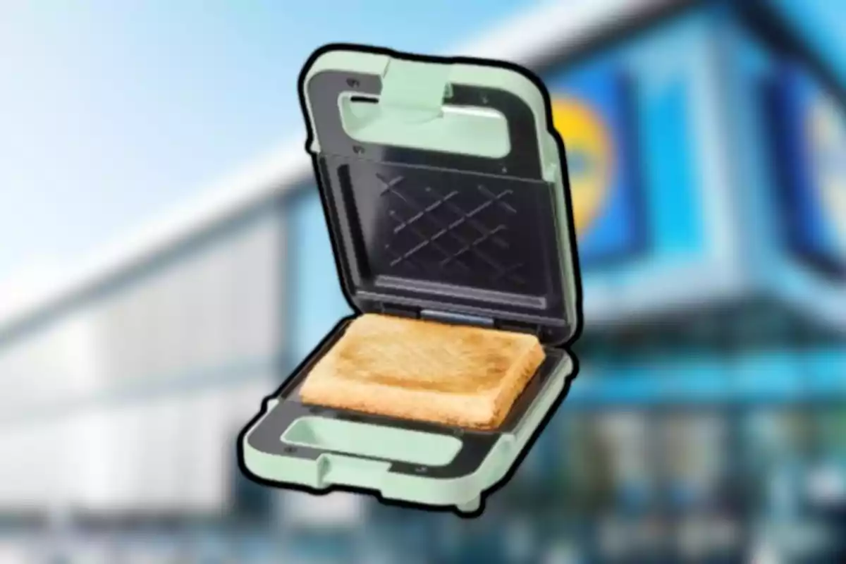 Sandwichera verde con un sándwich tostado en su interior frente a un edificio desenfocado Sandwichera verde con un sándwich tostado en su interior frente a un edificio desenfocado
