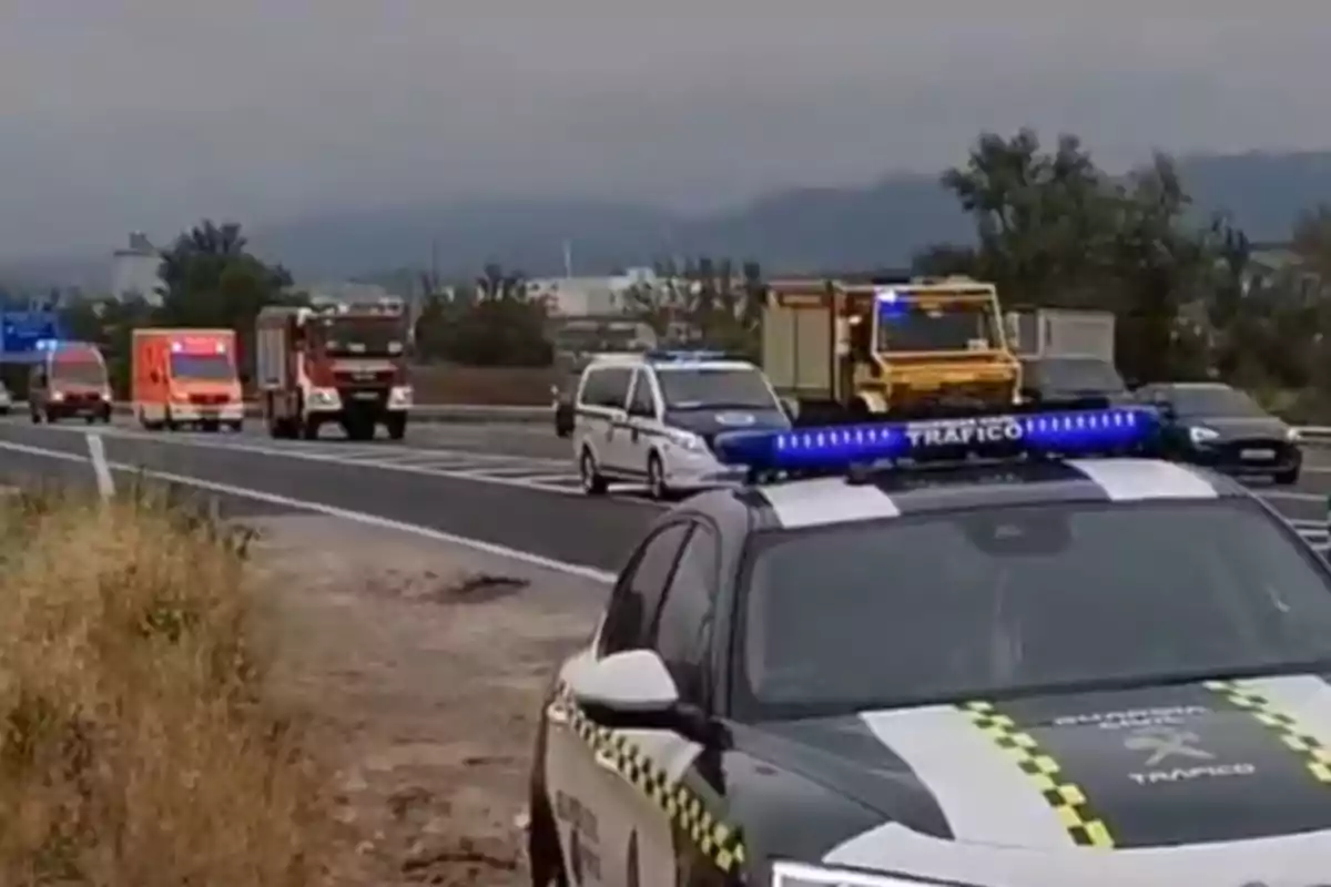 Varios vehículos de emergencia, incluyendo patrullas de tráfico, ambulancias y camiones de bomberos, están detenidos en una carretera bajo un cielo nublado. Varios vehículos de emergencia, incluyendo patrullas de tráfico, ambulancias y camiones de bomberos, están detenidos en una carretera bajo un cielo nublado.