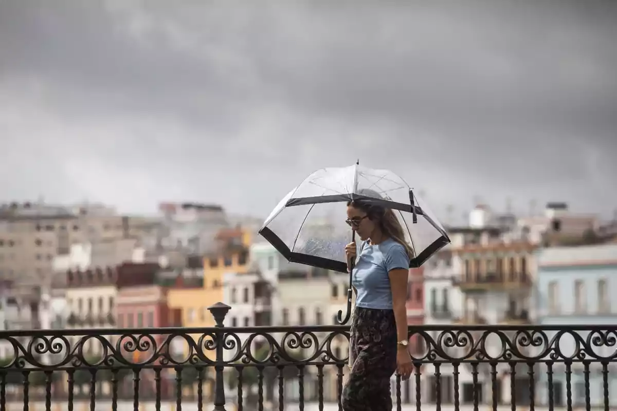 Mujer caminando bajo la lluvia con un paraguas transparente y edificios coloridos de fondo