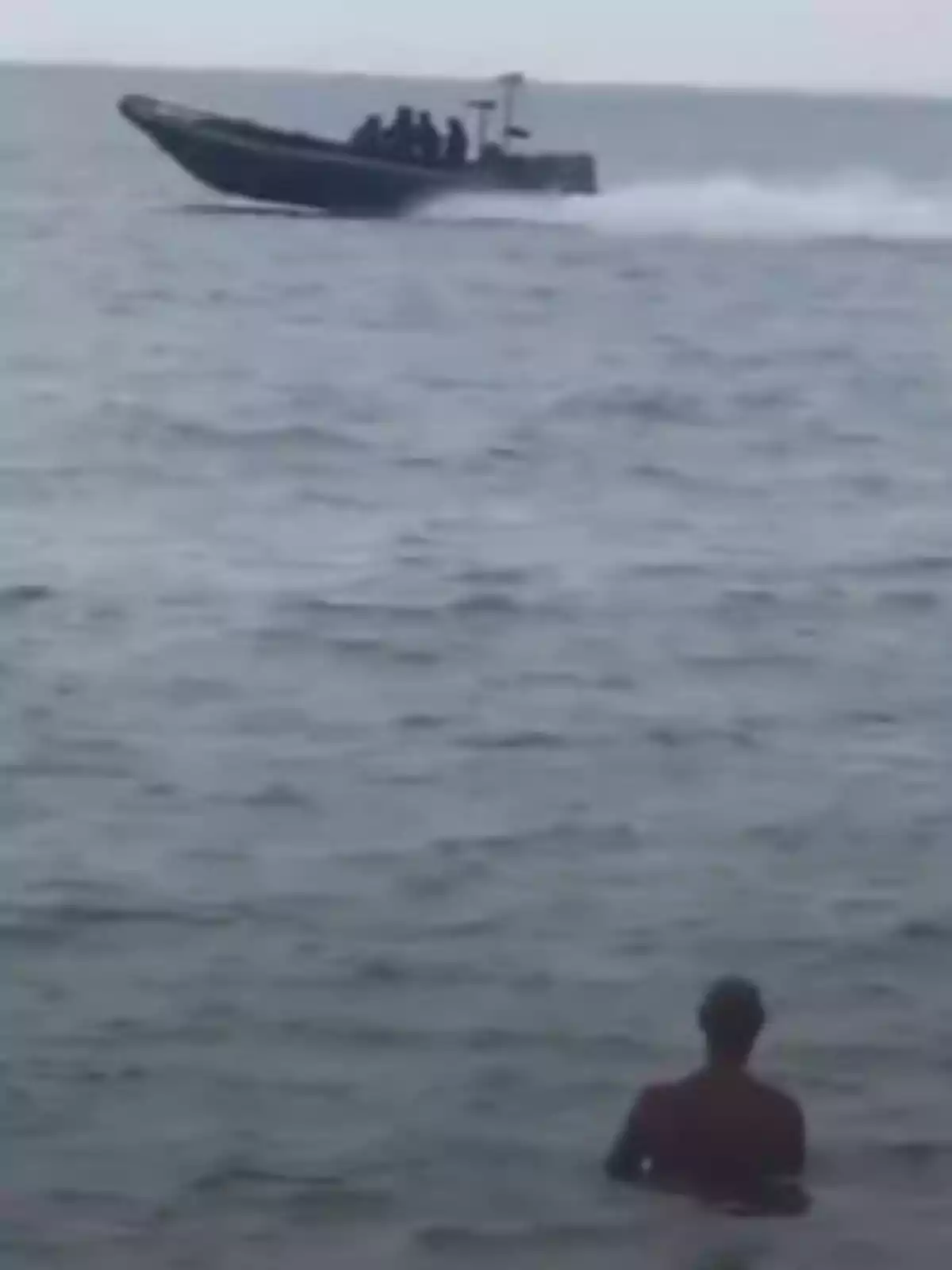 Persona dentro del mar observando una lancha rápida con varias personas a bordo pasando a lo lejos Persona dentro del mar observando una lancha rápida con varias personas a bordo pasando a lo lejos