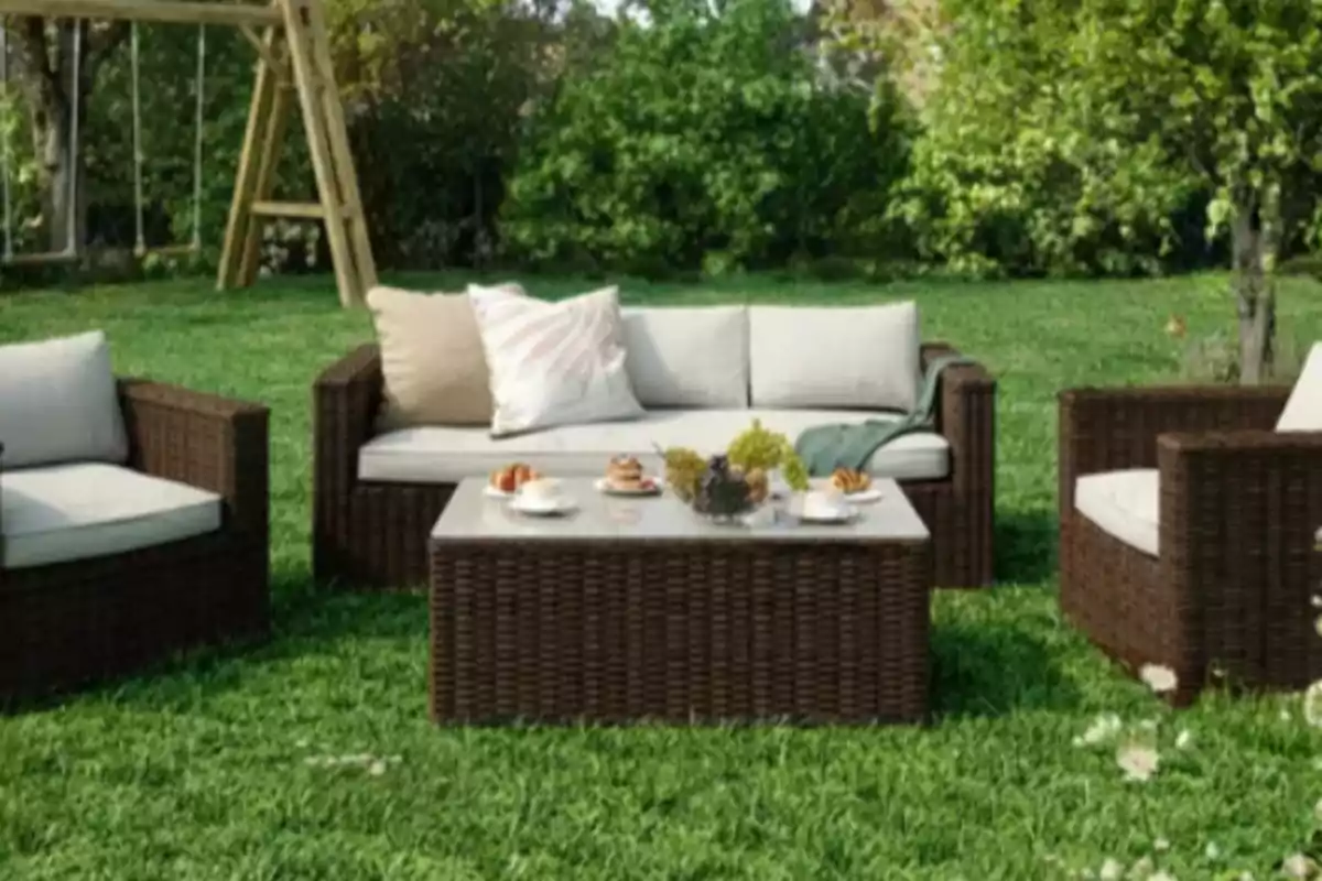 Juego de muebles de jardín de mimbre con cojines claros y una mesa con tazas y bocadillos sobre césped rodeado de árboles y un columpio de madera al fondo Juego de muebles de jardín de mimbre con cojines claros y una mesa con tazas y bocadillos sobre césped rodeado de árboles y un columpio de madera al fondo