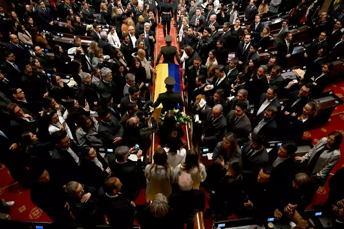 Vista aérea de una ceremonia fúnebre en un recinto oficial con un ataúd cubierto por una bandera y rodeado de personas vestidas de negro Vista aérea de una ceremonia fúnebre en un recinto oficial con un ataúd cubierto por una bandera y rodeado de personas vestidas de negro