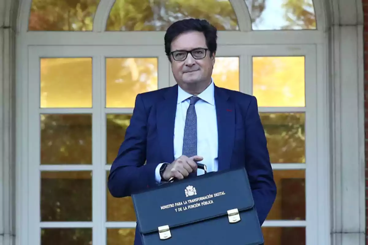 Hombre con gafas y traje azul sosteniendo un maletín negro frente a una puerta con ventanas Hombre con gafas y traje azul sosteniendo un maletín negro frente a una puerta con ventanas