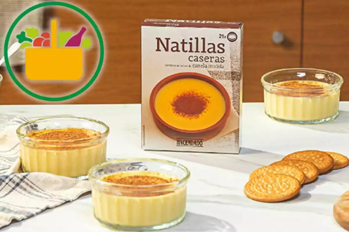 Postre de natillas caseras en recipientes de cristal junto a una caja del producto y varias galletas sobre una mesa blanca Postre de natillas caseras en recipientes de cristal junto a una caja del producto y varias galletas sobre una mesa blanca