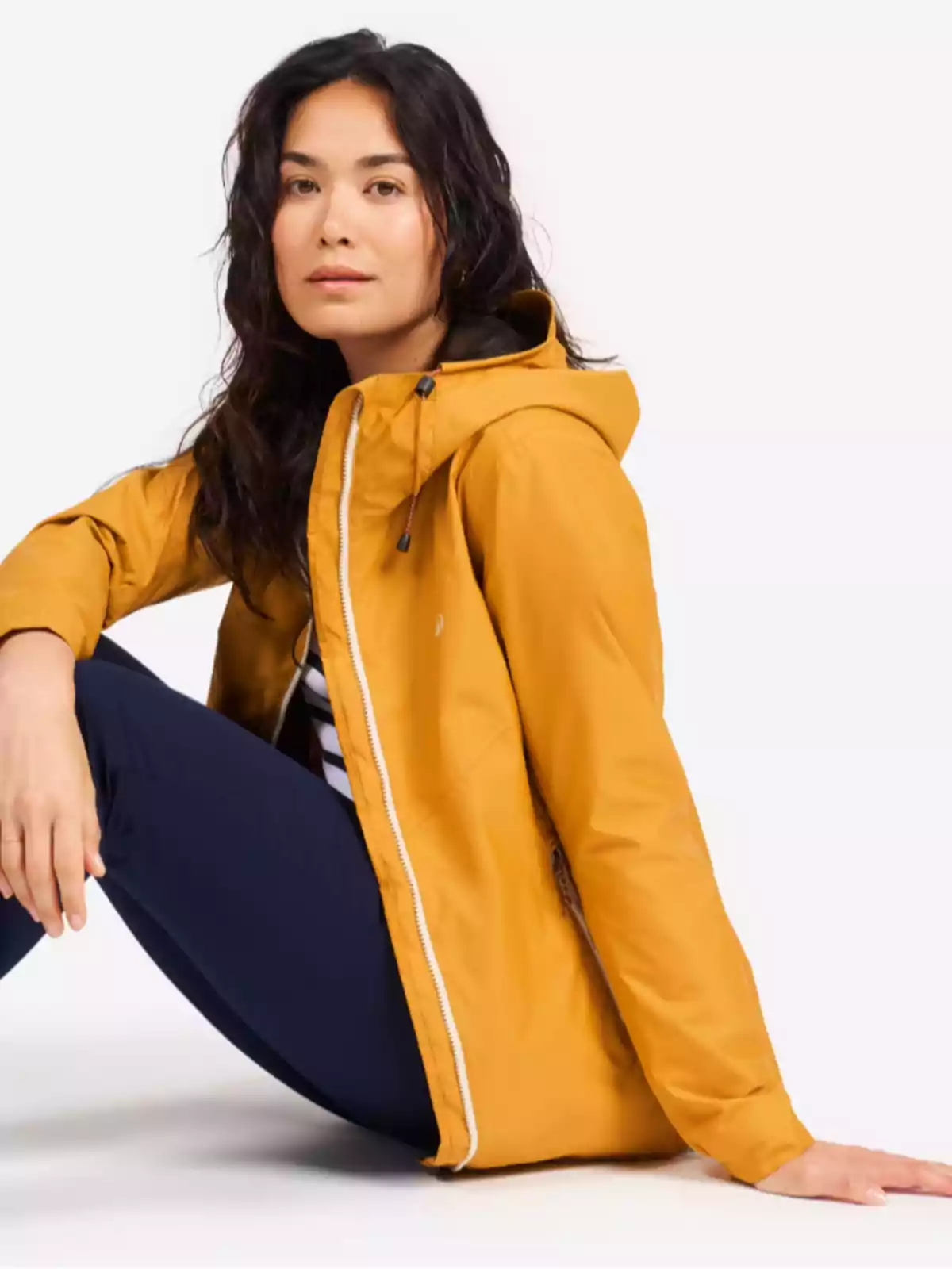 Mujer sentada con chaqueta amarilla y pantalón azul marino sobre fondo blanco Mujer sentada con chaqueta amarilla y pantalón azul marino sobre fondo blanco