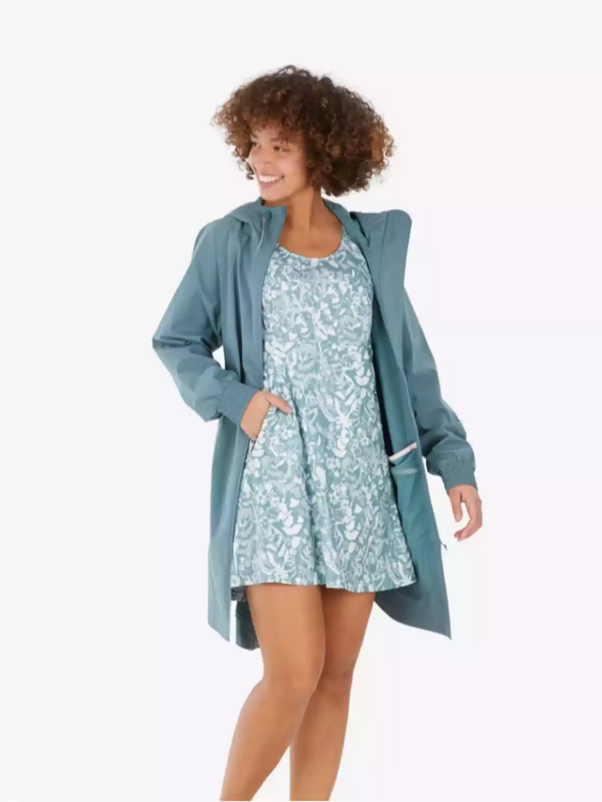 Mujer sonriente con cabello rizado lleva un vestido corto estampado en tonos verdes y una chaqueta larga azul claro Mujer sonriente con cabello rizado lleva un vestido corto estampado en tonos verdes y una chaqueta larga azul claro