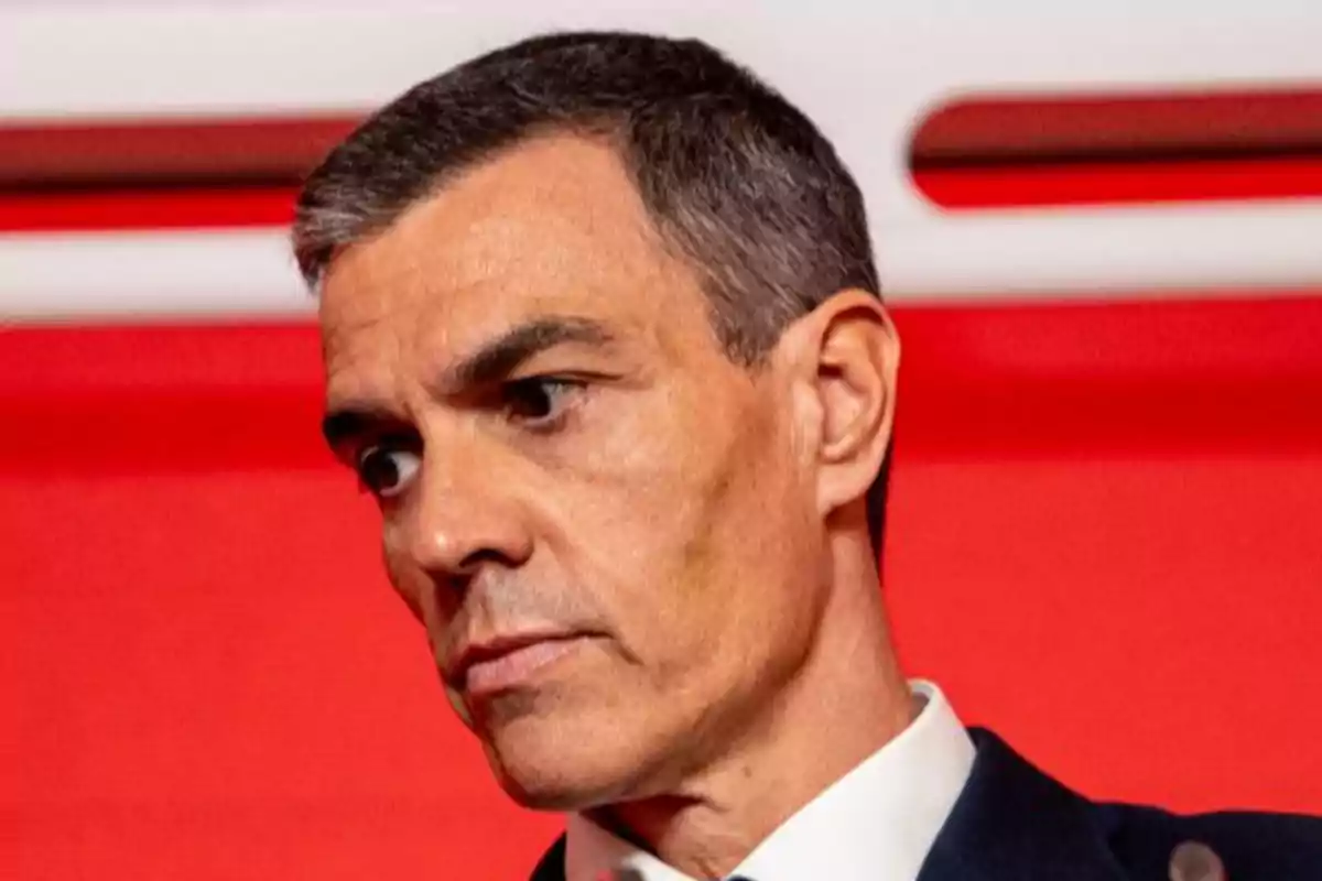 Hombre de cabello corto y canoso con expresión seria frente a un fondo rojo Hombre de cabello corto y canoso con expresión seria frente a un fondo rojo