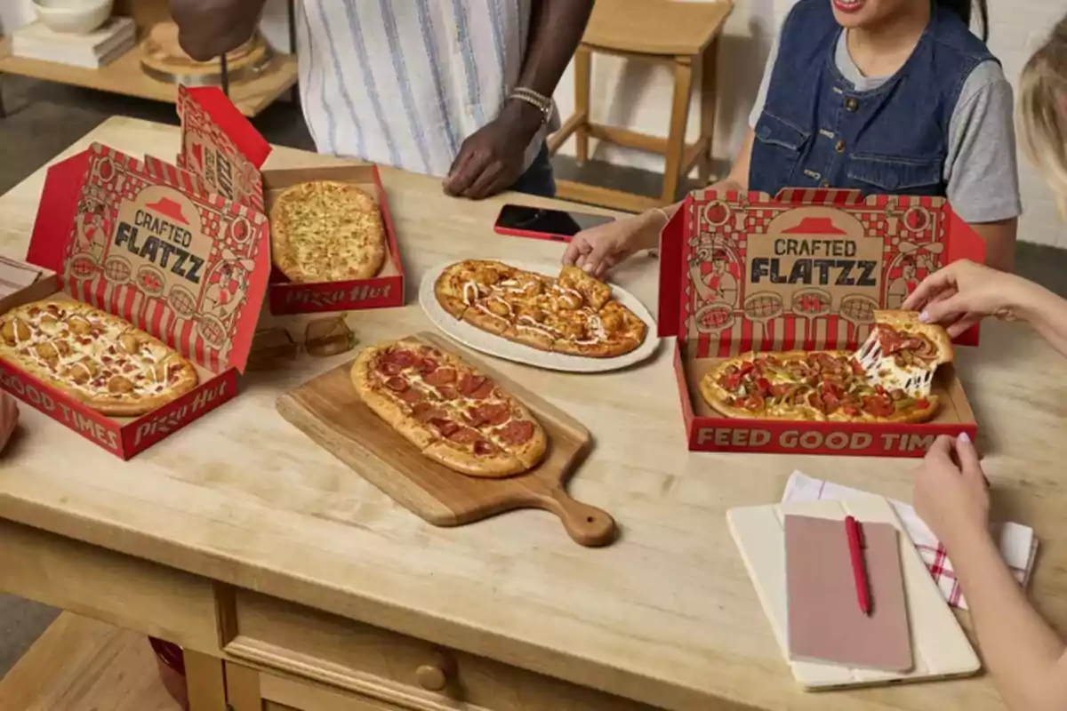 Several people enjoy different types of rectangular pizzas from Pizza Hut on a wooden table. Several people enjoy different types of rectangular pizzas from Pizza Hut on a wooden table.