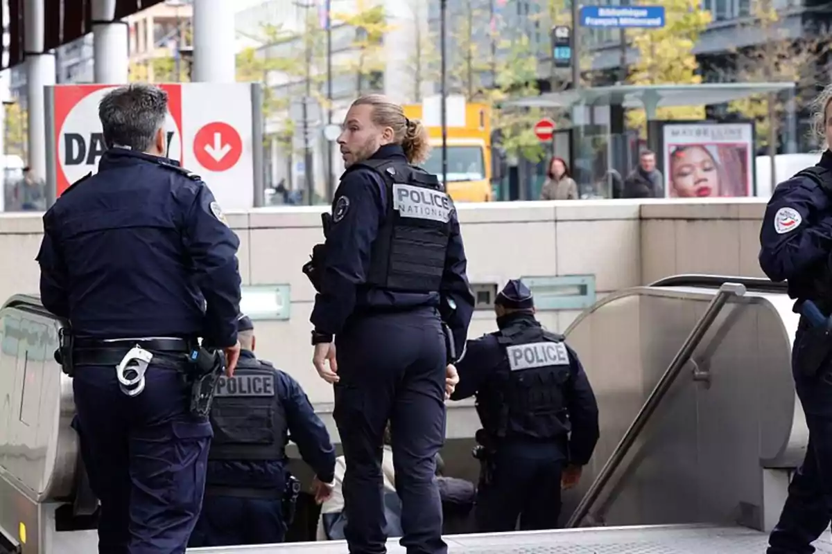 Varios policías con chalecos antibalas y uniformes oscuros bajan por unas escaleras eléctricas en una estación urbana