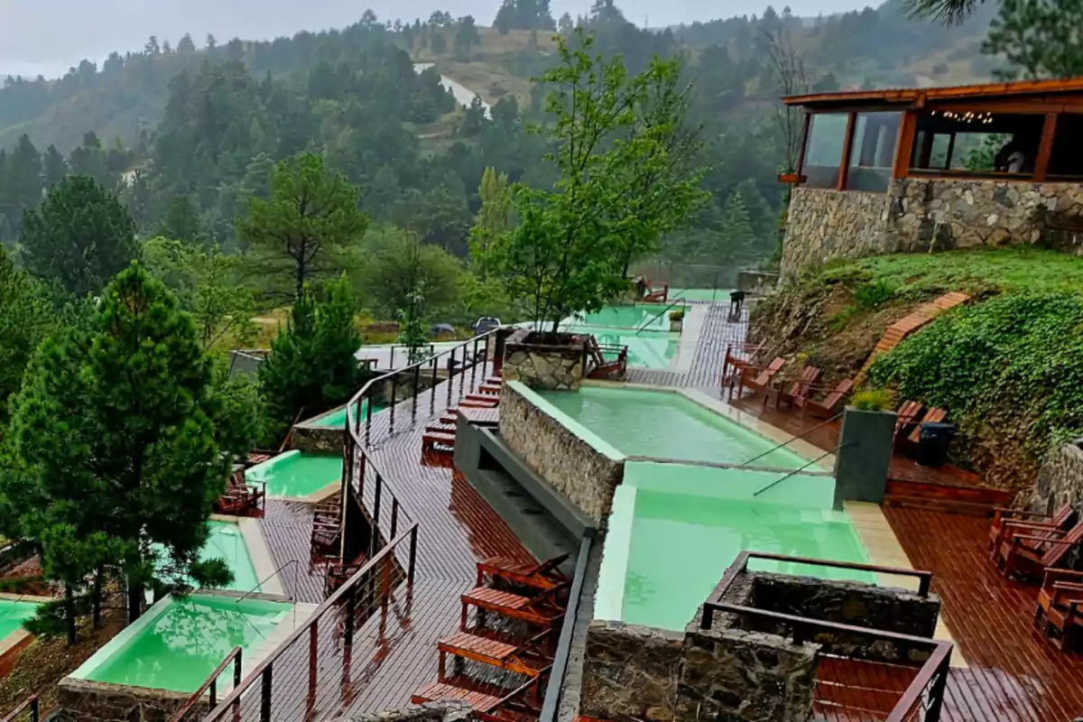 Piscinas termales al aire libre rodeadas de árboles y montañas con terrazas de madera y sillas para descansar Piscinas termales al aire libre rodeadas de árboles y montañas con terrazas de madera y sillas para descansar