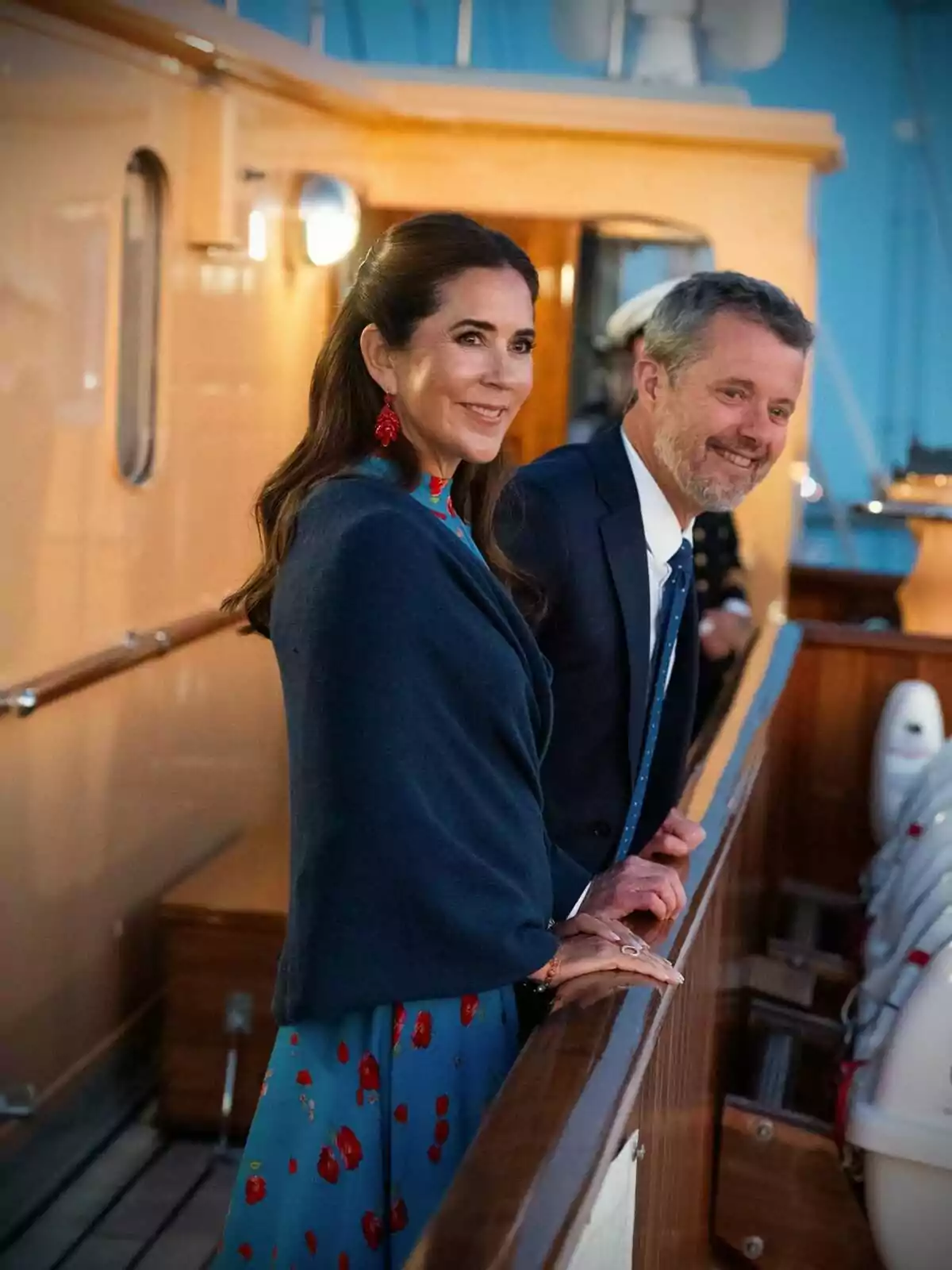 Mary and Frederik of Denmark, elegantly dressed, smile as they stand on the deck of a boat. Mary and Frederik of Denmark, elegantly dressed, smile as they stand on the deck of a boat.