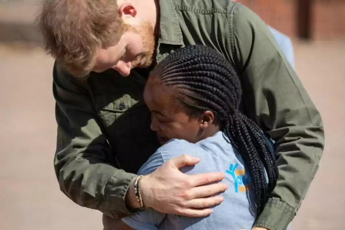 Un hombre con camisa verde abraza con cariño a una mujer de cabello trenzado que lleva puesta una camiseta gris Un hombre con camisa verde abraza con cariño a una mujer de cabello trenzado que lleva puesta una camiseta gris