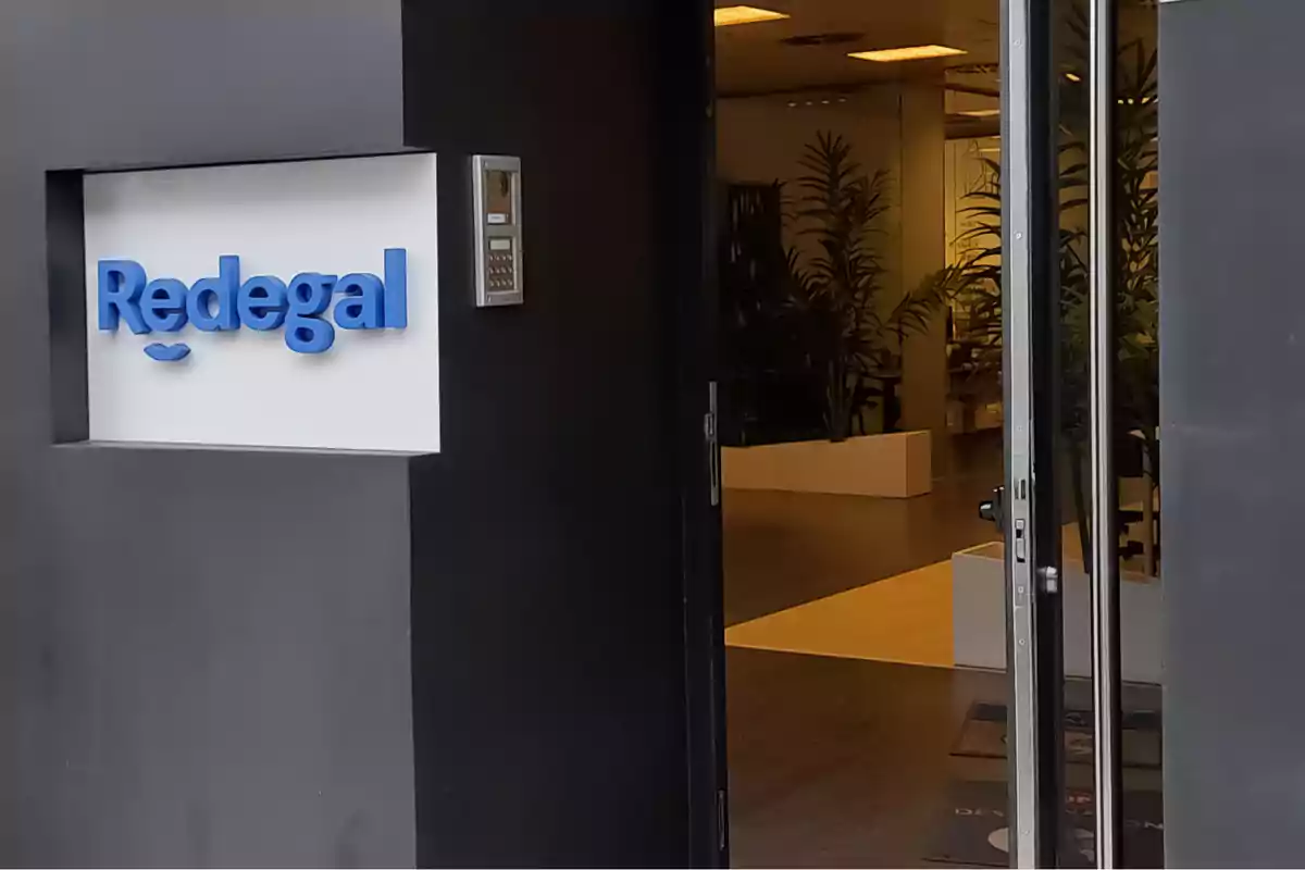 Entrada de una oficina con un letrero de Redegal en la pared y una puerta abierta que muestra plantas en el interior