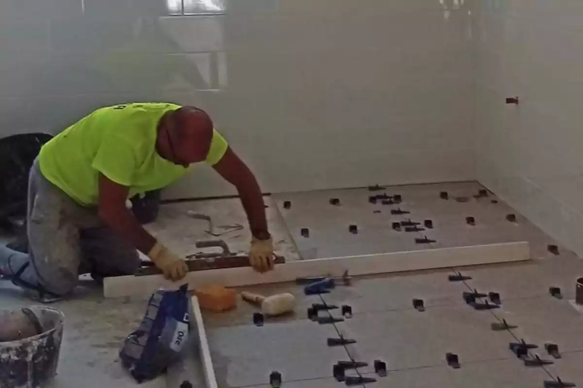 Hombre colocando losetas en el piso de una habitación usando herramientas y separadores de nivelación