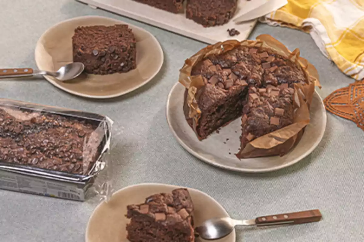 Varios pasteles de chocolate servidos en platos con cucharas sobre una mesa, uno de ellos en su envase y otro cortado en rebanadas Varios pasteles de chocolate servidos en platos con cucharas sobre una mesa, uno de ellos en su envase y otro cortado en rebanadas