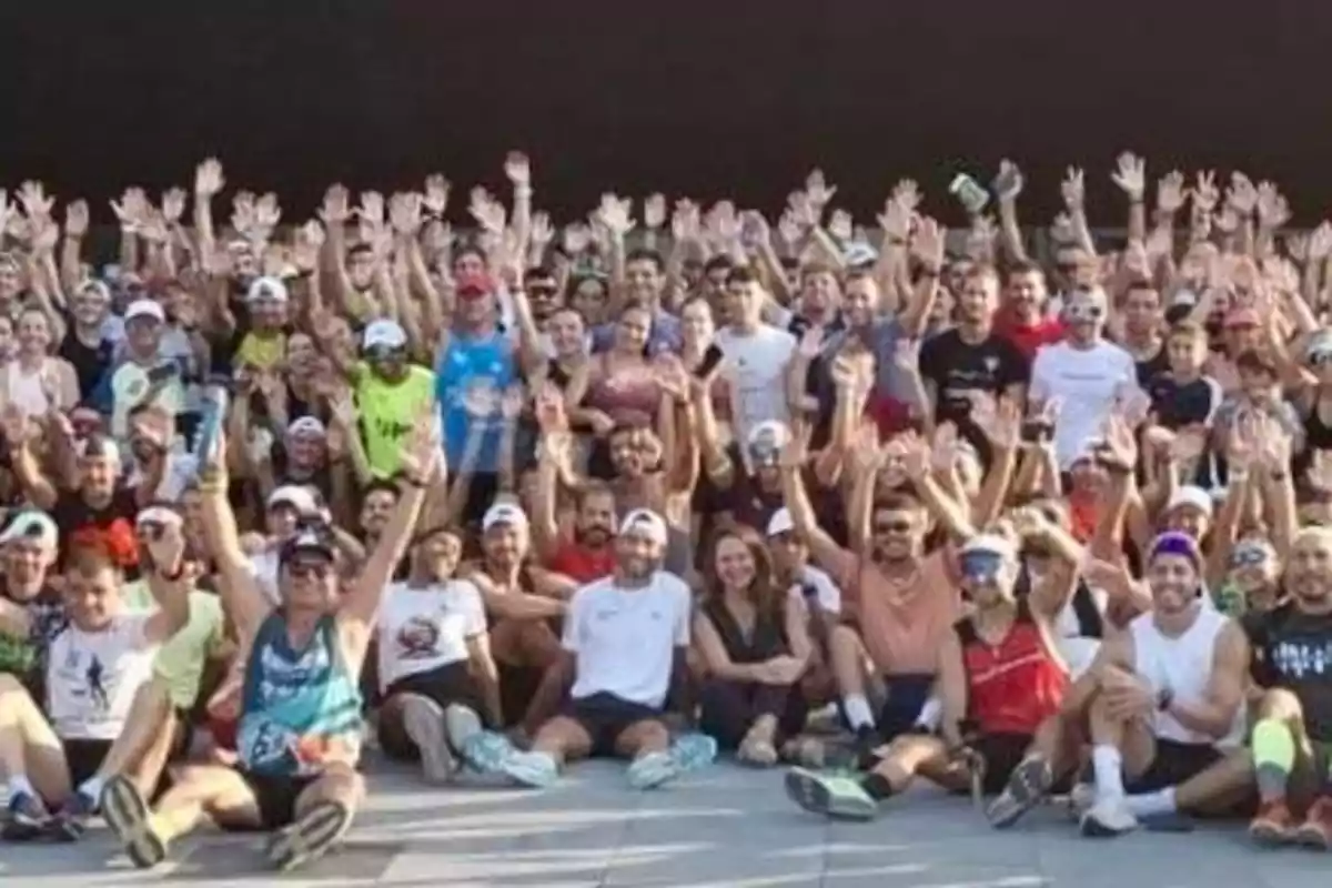 Grupo numeroso de personas reunidas al aire libre, la mayoría con ropa deportiva y levantando las manos, posando para una foto grupal Grupo numeroso de personas reunidas al aire libre, la mayoría con ropa deportiva y levantando las manos, posando para una foto grupal