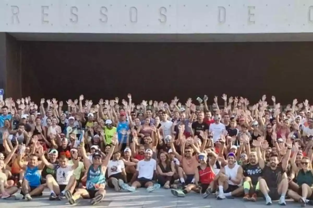 Grupo numeroso de personas reunidas al aire libre levantando las manos y sonriendo, la mayoría con ropa deportiva y gorras
