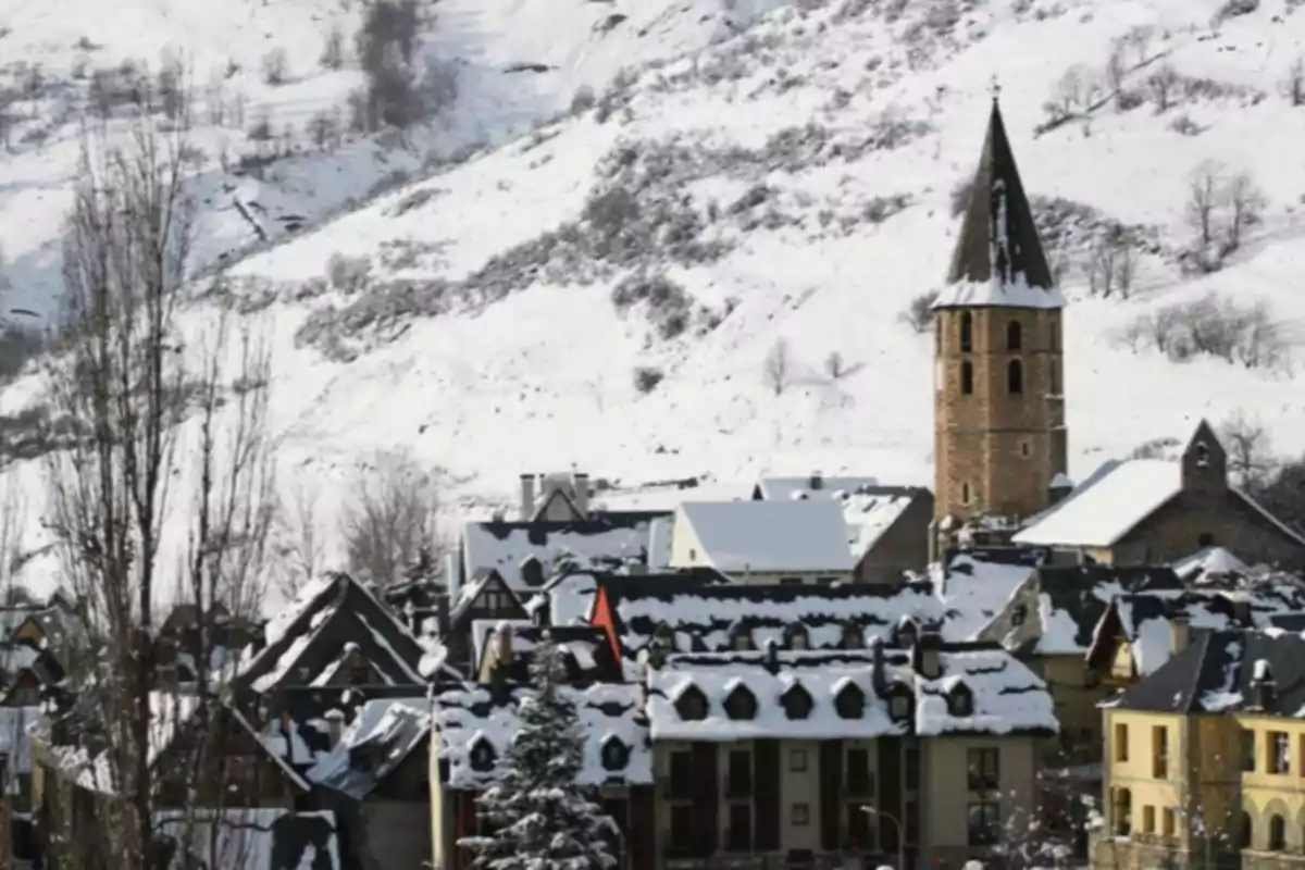 Pueblo de montaña con casas y tejados cubiertos de nieve y una iglesia con torre en invierno
