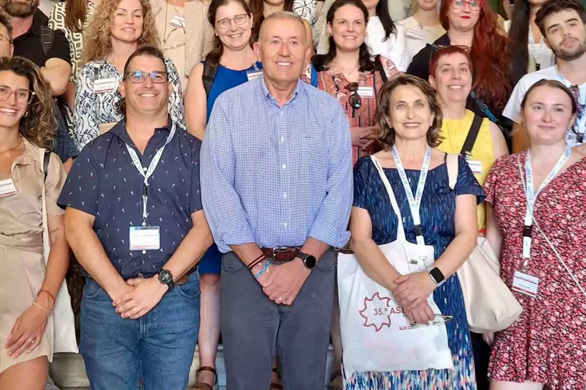 Grupo de personas posando y sonriendo en un evento profesional, varias llevan gafetes y bolsas de tela Grupo de personas posando y sonriendo en un evento profesional, varias llevan gafetes y bolsas de tela