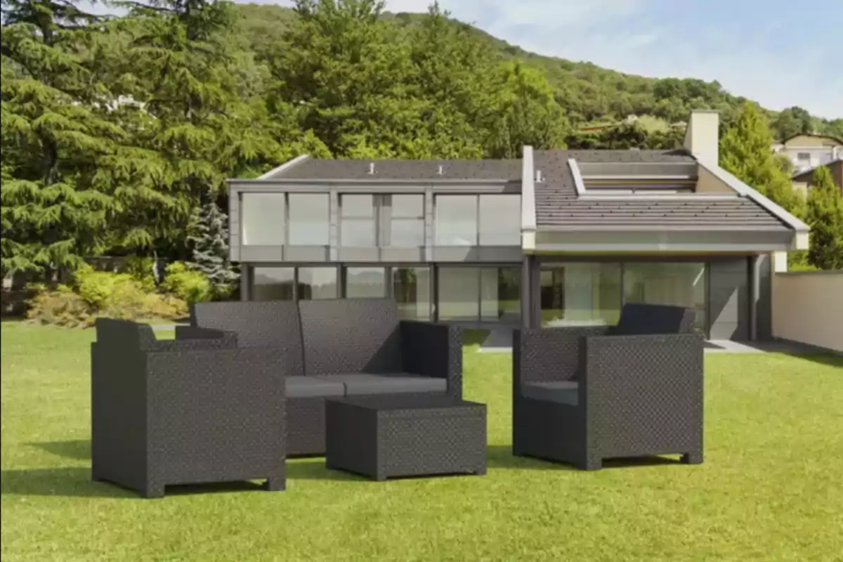Conjunto de muebles de jardín de color oscuro sobre césped frente a una casa moderna rodeada de árboles y vegetación Conjunto de muebles de jardín de color oscuro sobre césped frente a una casa moderna rodeada de árboles y vegetación