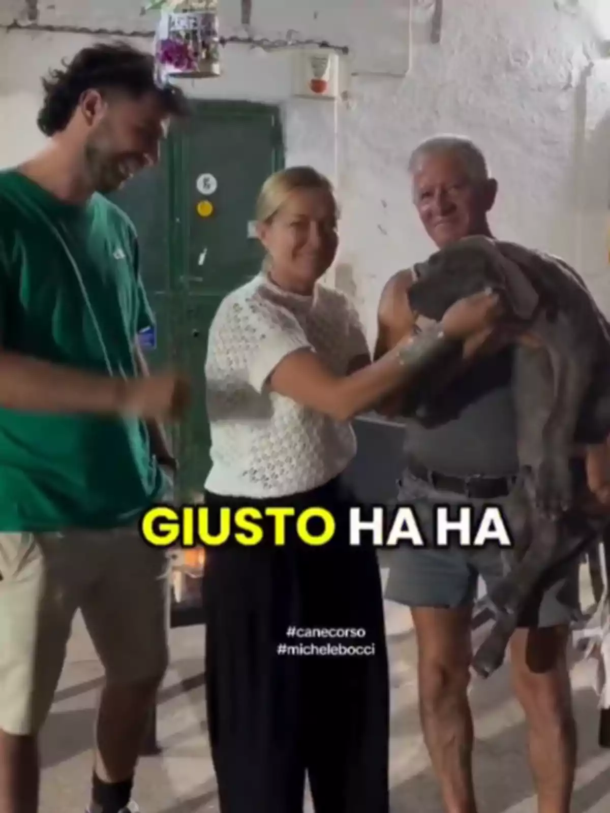 Tres personas sonríen mientras una de ellas sostiene un perro grande de color gris, con la palabra GIUSTO HA HA en letras amarillas y blancas sobre la imagen. Tres personas sonríen mientras una de ellas sostiene un perro grande de color gris, con la palabra GIUSTO HA HA en letras amarillas y blancas sobre la imagen.