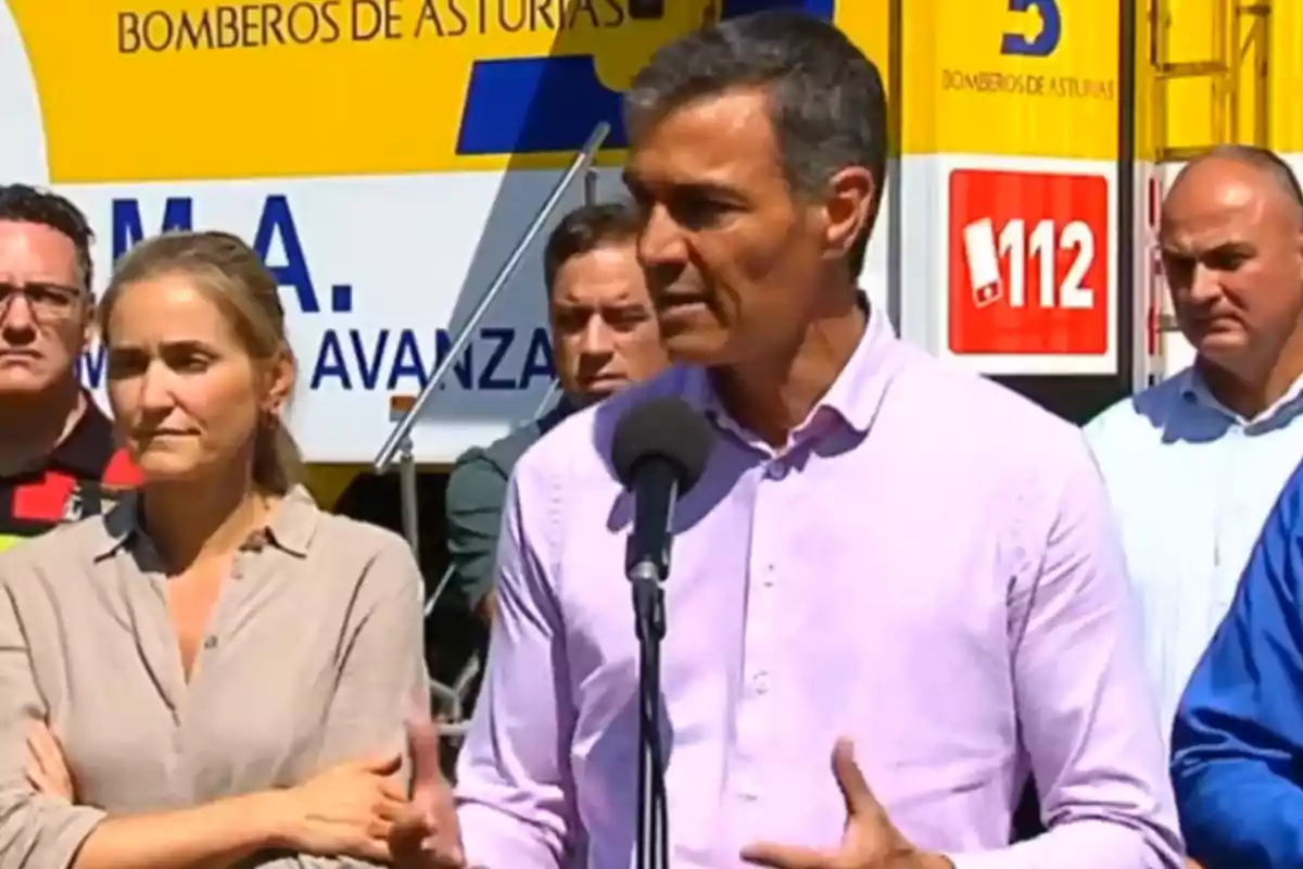 Un hombre con camisa clara habla frente a un micrófono mientras varias personas lo acompañan y al fondo se observa un vehículo de bomberos de Asturias con el número de emergencia 112 visible. Un hombre con camisa clara habla frente a un micrófono mientras varias personas lo acompañan y al fondo se observa un vehículo de bomberos de Asturias con el número de emergencia 112 visible.